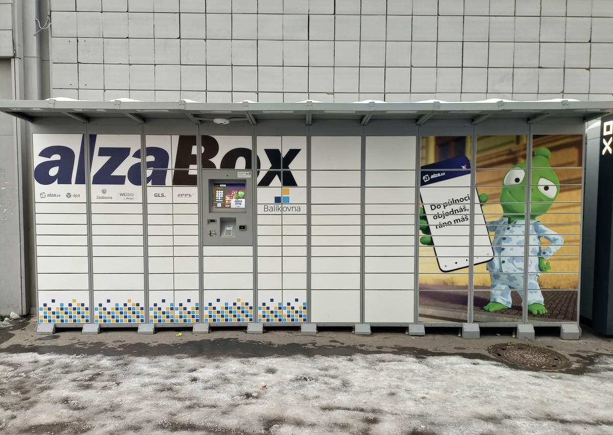 Bílá schránka AlzaBox se stříškou a ovládacím panelem u zdi v pražské ulici Španielova