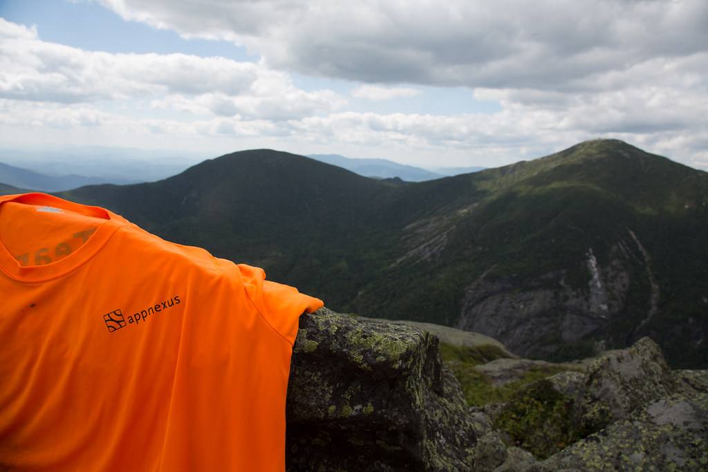 Oranžové tričko s logem AppNexus položené na skále nad horským údolím