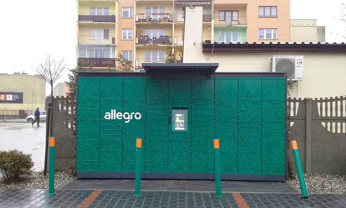 Oranžový výdejní box Allegro One Box na chodníku vedle obchodu
