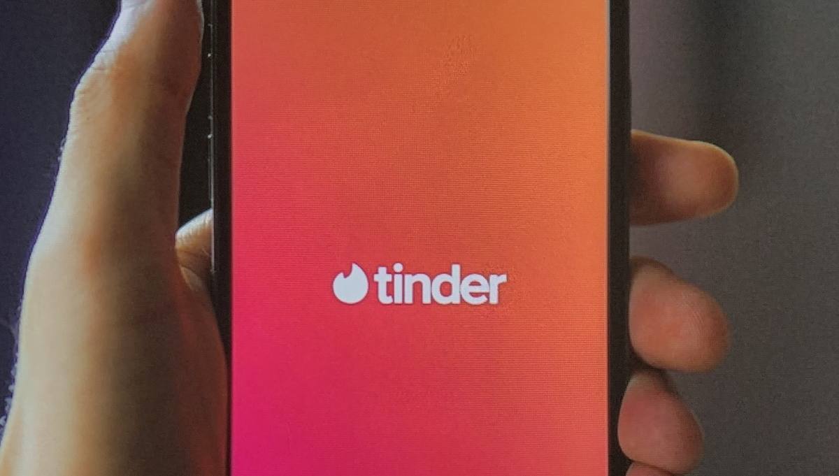 Ruka drží telefon s úvodní obrazovkou aplikace Tinder