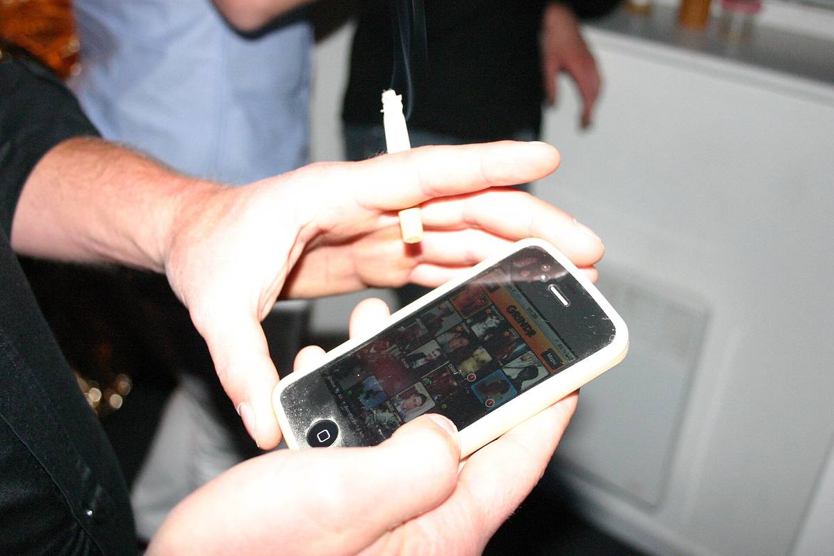Ruce drží iPhone s otevřenou mřížkou profilů v aplikaci Grindr