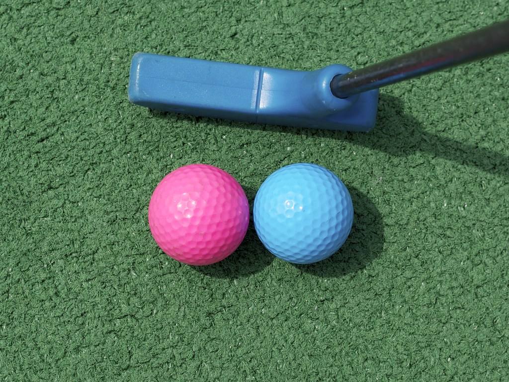 Hůl na minigolf a dva barevné míčky na umělém trávníku