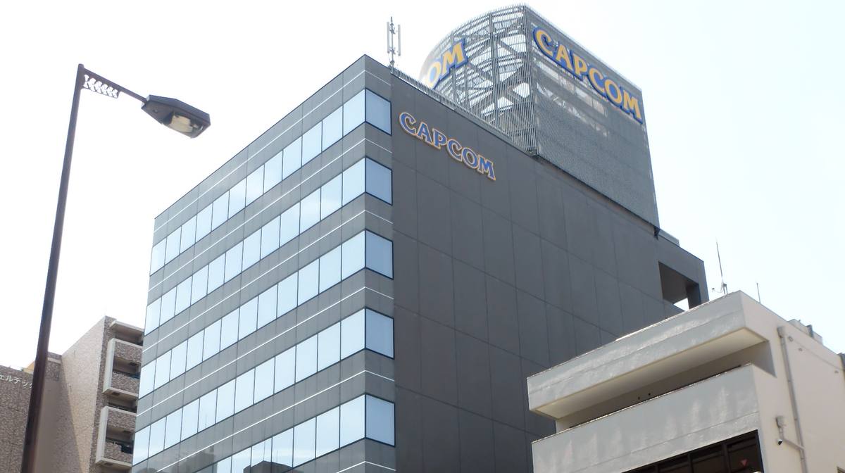 Šedá kancelářská budova s nápisem Capcom na fasádě a na kulaté konstrukci na střeše