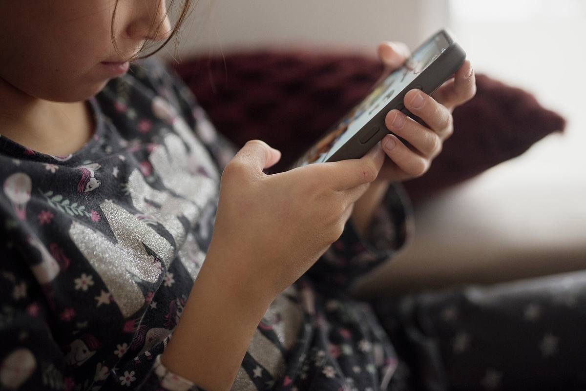 Dítě sedící na pohovce s mobilním telefonem v rukou