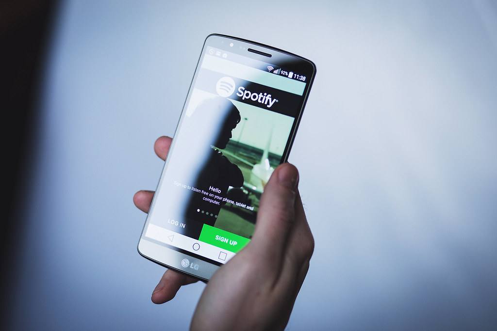 Ruka drží telefon s otevřenou aplikací Spotify