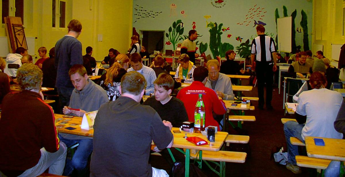 Hráči karetní hry Magic: The Gathering sedí proti sobě u dlouhých stolů na turnaji